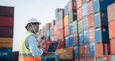Man With A Helmet And A Vest Looking Over Shipping Containers